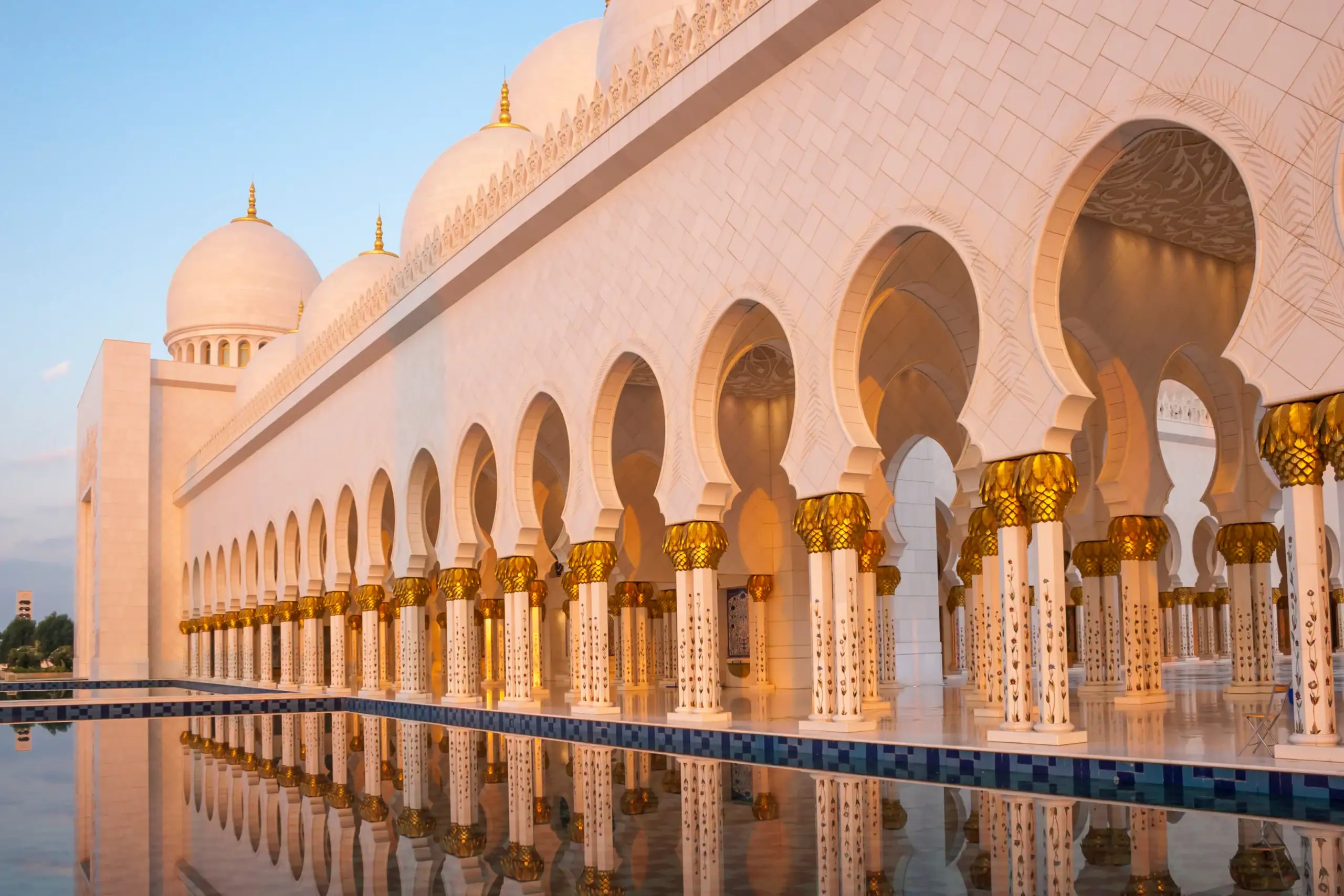 A white mosque with golden domes glows at sunset, its reflection embodying Islamic Burials New York serenity.