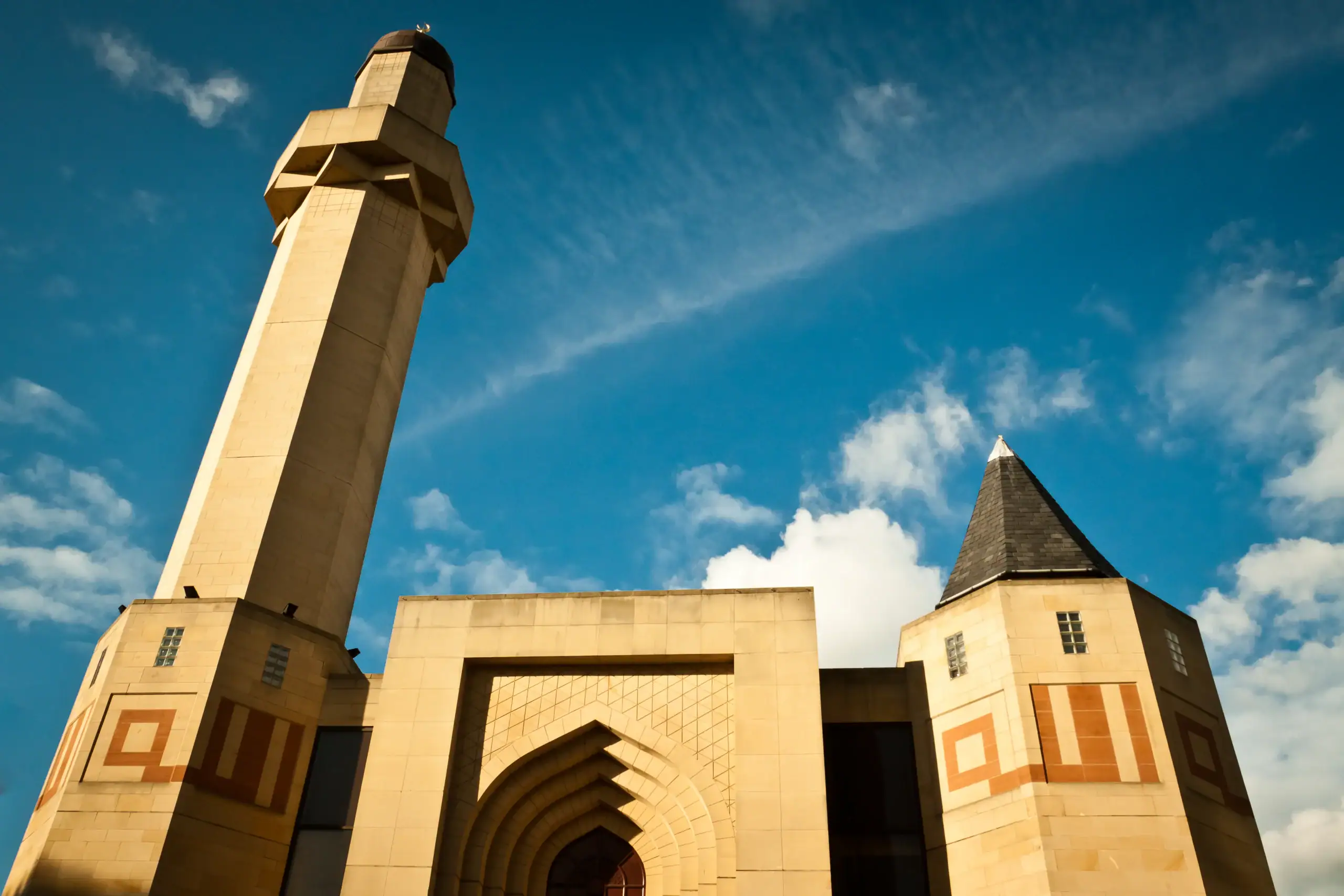 A mosque with a tall minaret and archway stands under blue skies near Islamic Funeral Services New York.