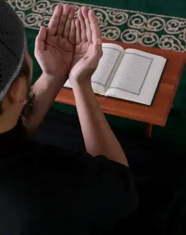 A person with raised hands prays before an open book, symbolizing Islamic Funeral Services New York.